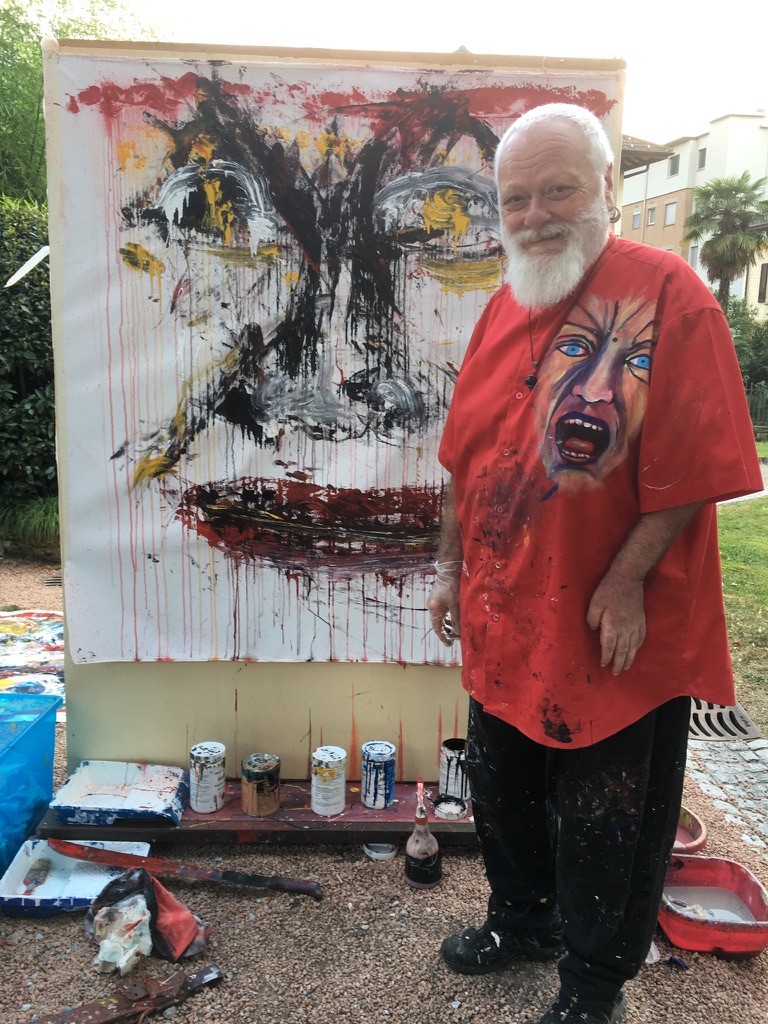 Nando Snozzi sorride davanti alla tela appena dipinta, un volto in nero, rosso e giallo, la camicia rossa macchiata di colore