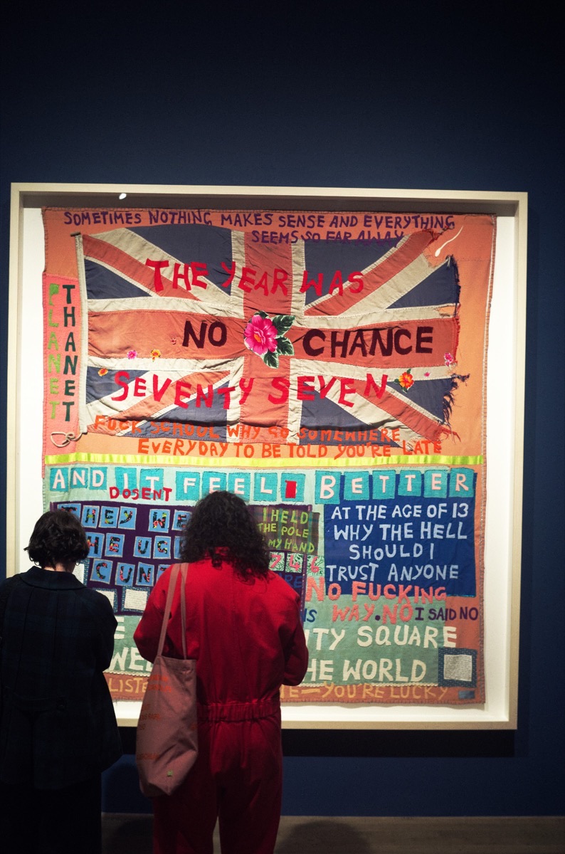 Zwei Besucherinnen stehen vor einer grossen Decke mit applizierten Worten in der Tate Modern, Mai 2026